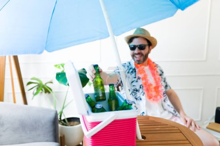 Foto de Primer plano de un hombre atractivo emocionado bebiendo una cerveza de un refrigerador mientras se divierten durante las vacaciones de verano fingiendo estar en la playa - Imagen libre de derechos