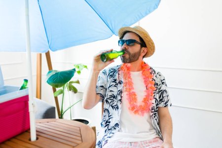 Photo for Handsome relaxed mid-adult man with sunglasses drinking a beer and enjoying a relaxing summer staycation at home - Royalty Free Image