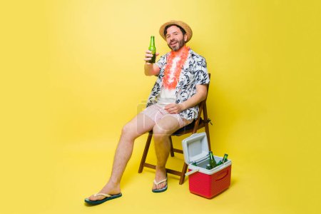 Foto de Hombre latino alegre haciendo contacto visual sonriendo mirando feliz diciendo vítores mientras bebe una cerveza en sus vacaciones de verano - Imagen libre de derechos
