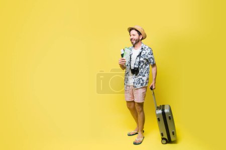 Photo for Happy caucasian man walking with a suitcase traveling to the beach during the summer against a yellow background with copy space - Royalty Free Image