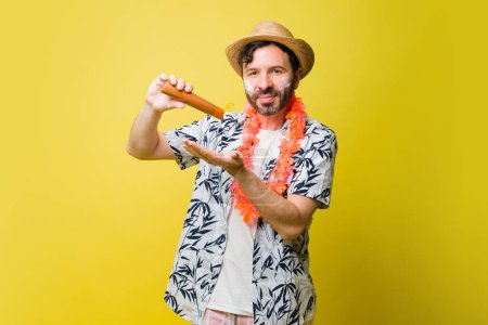 Photo for Smiling caucasian mid adult man putting on sunscreen while at the beach and making eye contact against a yellow background - Royalty Free Image