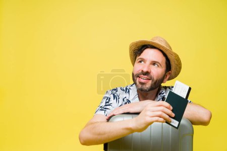 Téléchargez les photos : Pensé homme heureux dans la trentaine penser à voyager et des vacances tout en utilisant son passeport sur un fond jaune - en image libre de droit