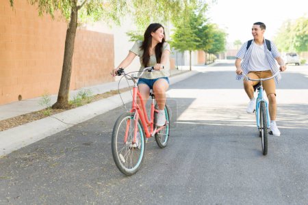 Photo for Happy young woman and man going on a bicycle ride during a date and having fun outdoors while laughing together - Royalty Free Image