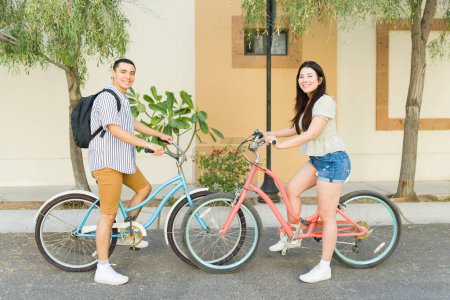 Photo for Full length of a happy attractive couple going on a date and riding their beautiful vintage bicycles carrying backpacks looking at the camera - Royalty Free Image