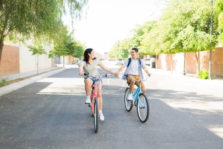 Photo for Beautiful couple holding hands during a fun summer date outdoors while riding vintage bicycles looking happy having fun - Royalty Free Image