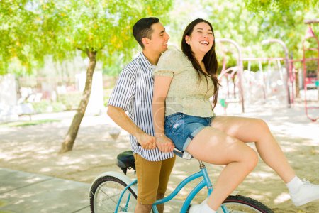 Téléchargez les photos : Couple très excité riant regardant heureux sur un rendez-vous tout en s'amusant à faire du vélo vintage dans le parc lors d'une belle journée d'été - en image libre de droit