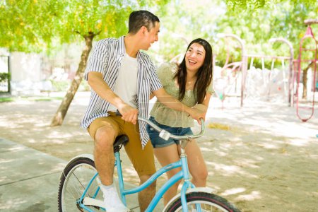 Photo for Happy caucasian man learning how to ride a bike with his cheerful attractive girlfriend and having fun together in the park - Royalty Free Image