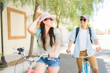 Foto de Preciosa mujer caucásica y hombre riendo juntos ir en una cita de verano y montar sus bicicletas al aire libre - Imagen libre de derechos