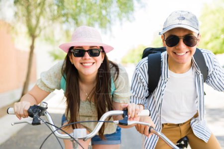 Photo for Fun girlfriend and boyfriend with sunglasses and hats smiling making eye contact and laughing during a bike ride outdoors during summer - Royalty Free Image