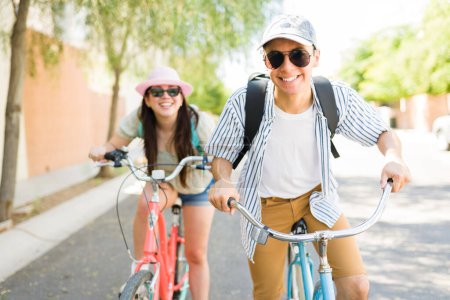 Photo for Handsome young man smiling looking happy with sunglasses and hat having fun riding a vintage bike with his happy girlfriend outdoors - Royalty Free Image
