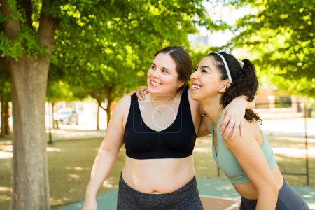 Photo for Relaxed plus size woman and her friend in her 30s hugging and smiling  while excited about their diverse workout in the park - Royalty Free Image