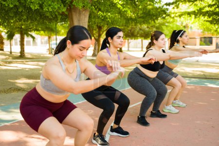 Téléchargez les photos : Groupe actif sportif de femmes dans la trentaine avec la diversité du corps et la positivité faire des exercices de squats dans le parc - en image libre de droit