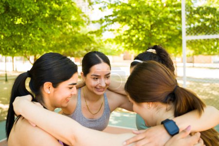Téléchargez les photos : Groupe diversifié de femmes souriant embrasser dans un cercle se préparant à commencer leur entraînement de remise en forme dans le parc tout en célébrant la positivité du corps - en image libre de droit