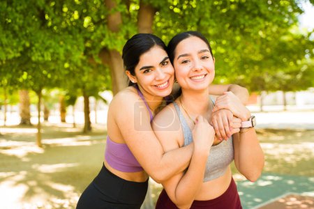 Téléchargez les photos : Attrayant sportif femmes amis dans leur trentaine étreignant et souriant regardant heureux avant de travailler à l'extérieur - en image libre de droit