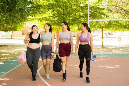 Foto de Longitud completa de atractivas mujeres diversas que usan ropa deportiva caminando juntas y disfrutando de un entrenamiento al aire libre o preparándose para ir a correr - Imagen libre de derechos