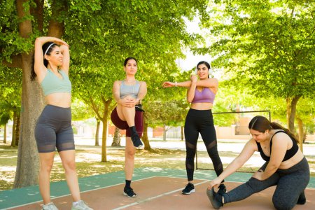 Photo for Happy diverse group of young women smiling and stretching their diverse bodies smiling while doing warm up exercises in the park - Royalty Free Image