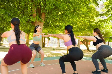 Téléchargez les photos : Plus la taille et les femmes minces avec divers corps faisant des exercices de squat lors d'un cours de fitness dans le parc et célébrant l'acceptation du corps - en image libre de droit