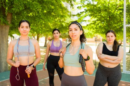 Téléchargez les photos : Groupe sportif de femmes célébrant la positivité et la diversité du corps en regardant la caméra prête à commencer à faire de l'exercice corde sautante à l'extérieur - en image libre de droit