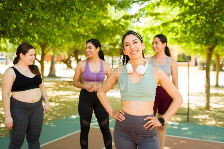 Téléchargez les photos : Femme sportive latine sportive avec écouteurs heureux de courir ou de faire de l'exercice avec son groupe diversifié de femmes amies à l'extérieur - en image libre de droit