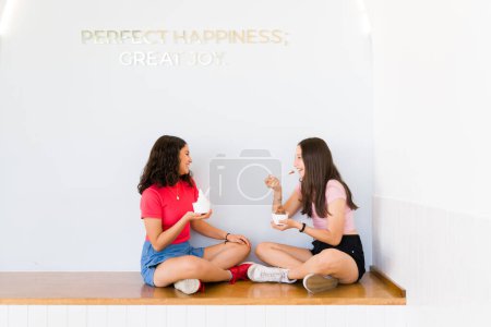 Photo for Cheerful teenagers sitting at the ice cream shop while talking and eating ice cream after buying frozen yogurt together - Royalty Free Image
