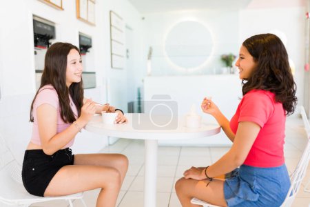 Foto de Sonriendo hermosas amigas adolescentes disfrutando del verano comiendo delicioso helado en la tienda de yogures congelados y divirtiéndose - Imagen libre de derechos