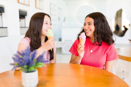 Photo for Cheerful happy teen girls enjoying talking while eating an ice cream cone while going to the frozen yogurt shop together and having fun - Royalty Free Image