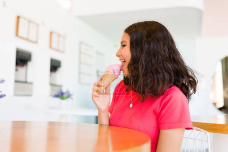Téléchargez les photos : Profil d'une adolescente heureuse et jeune fille gaie tout en appréciant de manger un délicieux cône de crème glacée en été à la boutique de gelato - en image libre de droit
