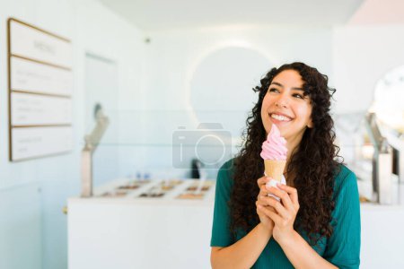 Photo for Excited young woman laughing while enjoying eating an ice cream cone at the frozen yogurt shop looking very happy - Royalty Free Image
