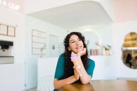 Foto de Mujer joven y relajada que se ve muy feliz y relajante mientras está sentada comiendo delicioso helado o helado durante el verano - Imagen libre de derechos