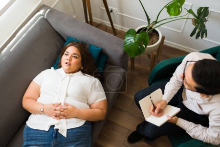 Téléchargez les photos : Femme détendue allongée sur le canapé et écoutant une méditation guidée en thérapie avec un psychologue pour sa dépression et son anxiété - en image libre de droit