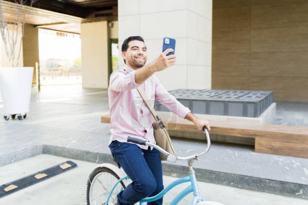 Photo for Happy handsome man taking a selfie with her smartphone for social media while commuting to work riding his bicycle - Royalty Free Image