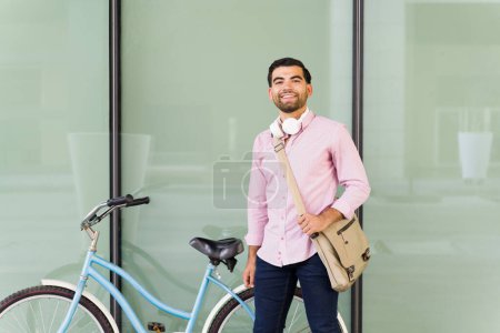 Téléchargez les photos : Joyeux homme heureux prêt à travailler dans un bâtiment urbain arrivant en vélo pendant son trajet - en image libre de droit