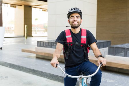 Foto de Happy food delivery worker sonriendo haciendo contacto visual luciendo alegre mientras monta su bicicleta haciendo recados - Imagen libre de derechos