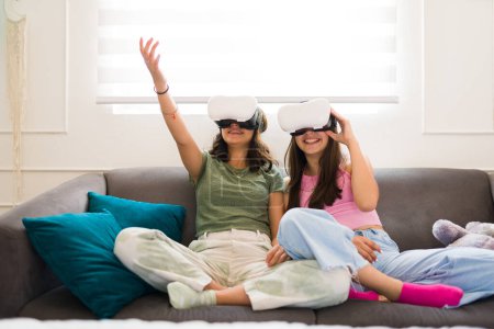 Foto de Emocionados adolescentes y amigos que usan gafas de realidad virtual y ven un video de tecnología mientras se sientan juntos en el sofá - Imagen libre de derechos