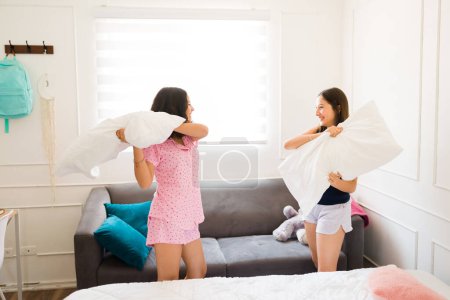 Photo for Excited teen girls in pajamas laughing and having fun with a pillow fight during pajamas sleepover - Royalty Free Image