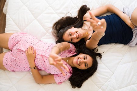 Photo for High angle of happy beautiful teenage girls lying in bed and laughing having fun during a sleepover - Royalty Free Image