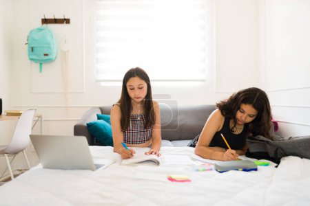 Téléchargez les photos : Les adolescentes et les meilleurs amis font leurs devoirs ou étudient ensemble en utilisant l'ordinateur portable dans leur chambre - en image libre de droit