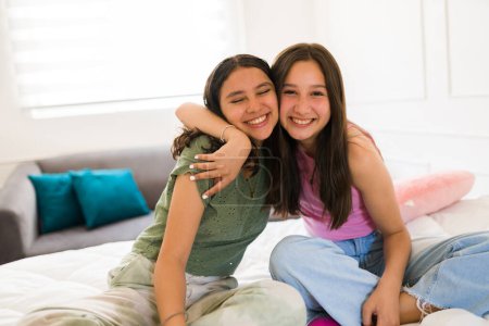 Photo for Cheerful happy teenage girls and best friends hugging and smiling while making eye contact having fun in the bedroom - Royalty Free Image
