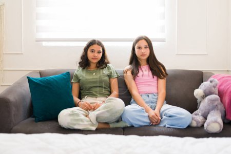 Photo for Caucasian teen girl with her hispanic best friend sitting together relaxing on the sofa while hanging out in the bedroom - Royalty Free Image