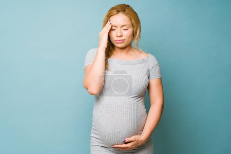 Photo for Caucasian pregnant woman in her 30s feeling unwell and suffering from migraine during pregnancy - Royalty Free Image