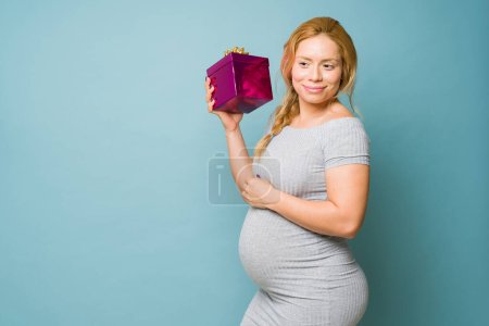 Foto de Hermosa mujer recibiendo regalos durante el embarazo y sacudiendo una caja de regalo para tratar de adivinar lo que hay dentro - Imagen libre de derechos
