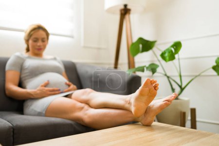 Photo for Pregnant woman in her 30s suffering from swollen feet and resting her feet at home - Royalty Free Image