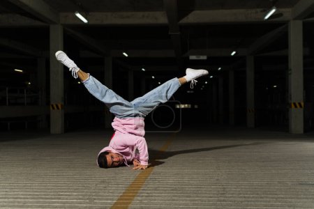 Foto de Hombre hispano y artista callejero bailando break dance estilo libre en un garaje oscuro y haciendo una actuación moderna - Imagen libre de derechos