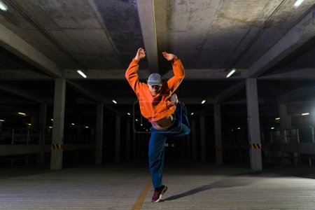 Téléchargez les photos : Artiste urbain talentueux dansant et faisant une danse de street freestyle dans un garage sombre - en image libre de droit