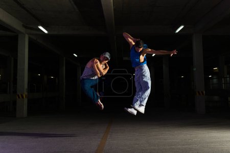 Téléchargez les photos : Danseurs de rue hispaniques actifs sautant dans les airs tout en dansant sur de la musique cool funky et en faisant une danse urbaine freestyle - en image libre de droit