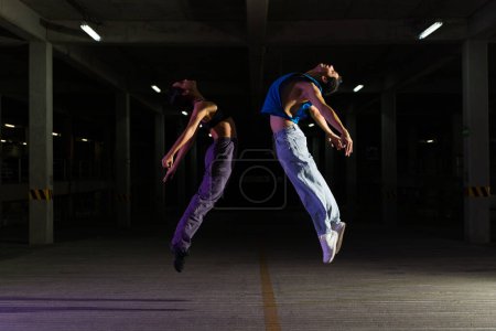 Téléchargez les photos : Couple latin talentueux et danseurs de rue sautant tout en dansant et en exécutant une chorégraphie de danse moderne urbaine - en image libre de droit