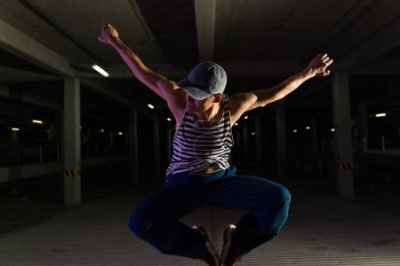 Téléchargez les photos : Homme latino attrayant et danseur de rue urbain sautant tout en dansant faisant une danse moderne cool la nuit - en image libre de droit