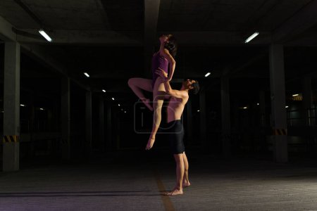 Téléchargez les photos : Jeune homme artistique portant en l'air une femme latine en justaucorps tout en dansant le ballet classique moderne dans la rue - en image libre de droit