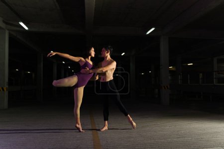 Photo for Beautiful couple dancing classical ballet at night at a dark parking lot and doing an artistic performance together - Royalty Free Image
