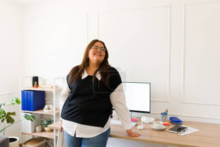 Téléchargez les photos : Grande femme d'affaires hispanique détendue se sentant excitée tout en riant et en appréciant son travail de bureau - en image libre de droit